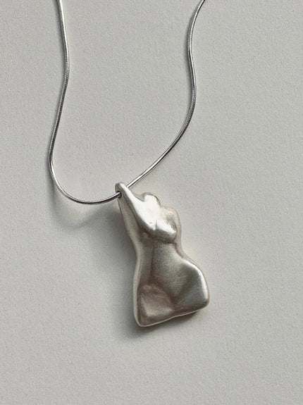 The Divine Feminine Necklace features a pendant shaped like an abstract human torso, crafted from reclaimed sterling silver, shown on a plain light gray background.